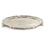 An early 20th century silver salver of circular form with piecrust border on three outswept feet,
