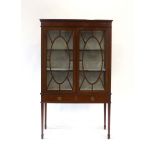 An Edwardian mahogany, strung and glazed two-door display cabinet on tapering legs with block feet,