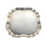 An early 20th century silver salver of square form with piecrust border on four outswept feet,