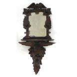 A Black Forest-type carved wall mirror with a shelf and figural support, h.