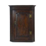 An 18th century oak hanging corner cabinet with a single panelled door, w.