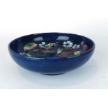 A Moorcroft shallow dish of circular form, decorated with orchids on a mottled blue ground,