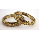 A pair of Indian yellow metal bangles with pierced decoration and set white and pink glass,