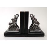 A pair of ebonised bookends of book form each mounted with a metalware elephant, its trunk raised,