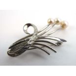 A silver brooch in the form of a floral spray set three graduated cultured pearls, w. 4.