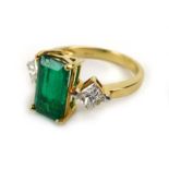 An 18ct yellow gold ring set emerald cut emerald within a raised four claw setting,