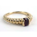 An 18ct yellow gold ring set oval ruby within a raised rubover setting within a beaded shank,