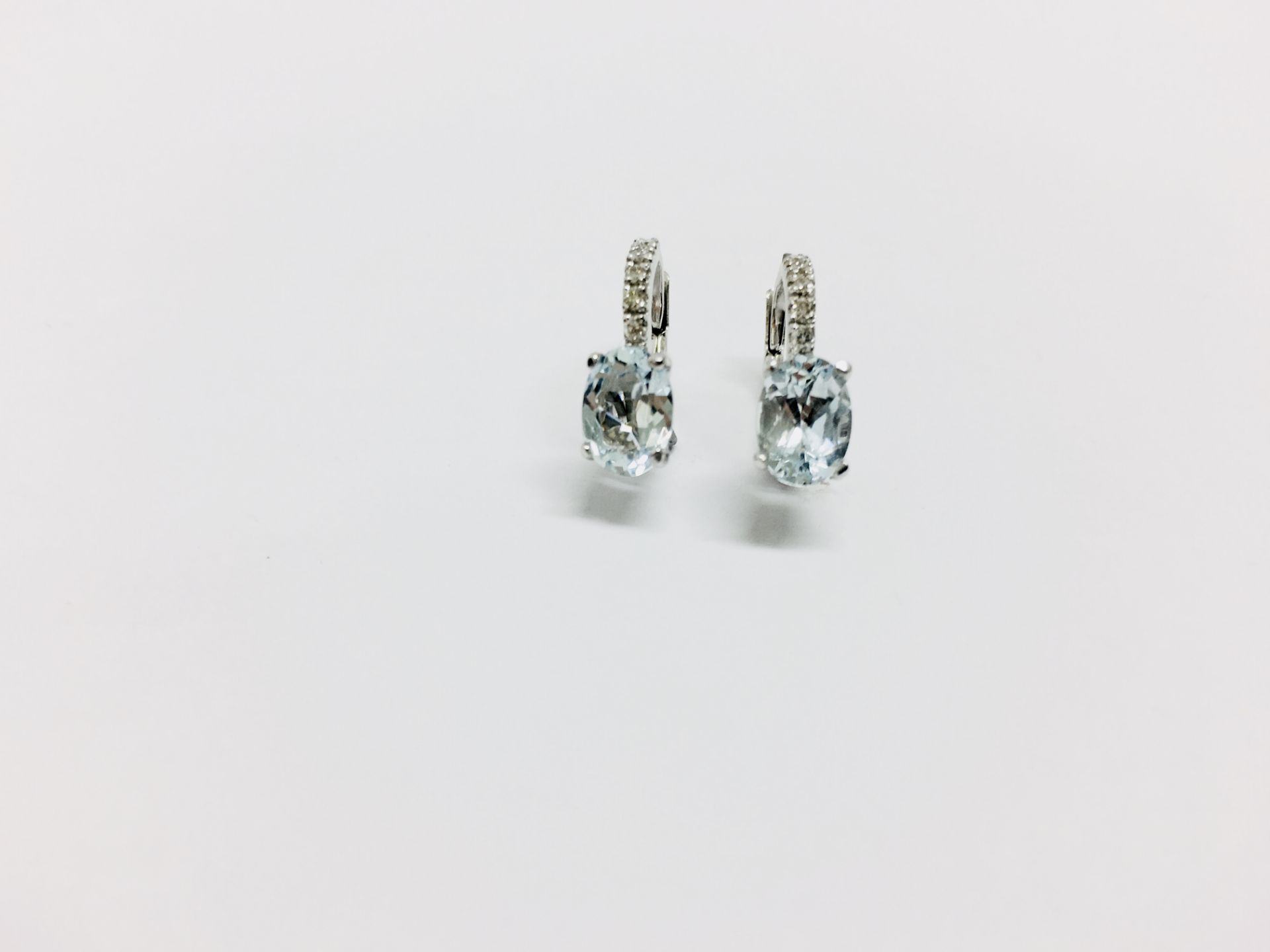 1.60ct Aqua marine and diamond hoop style earrings. Each is set with a 7x 5mm oval cut aqua (