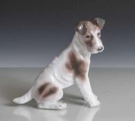 Kleiner sitzender Terrier aus Porzellan, farbig schraffiert, unbek. Porzellanmarke. H: ca. 14,5cm.
