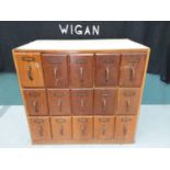 A retro mid 20th century index card filing cabinet comprised of three rows of five drawers.