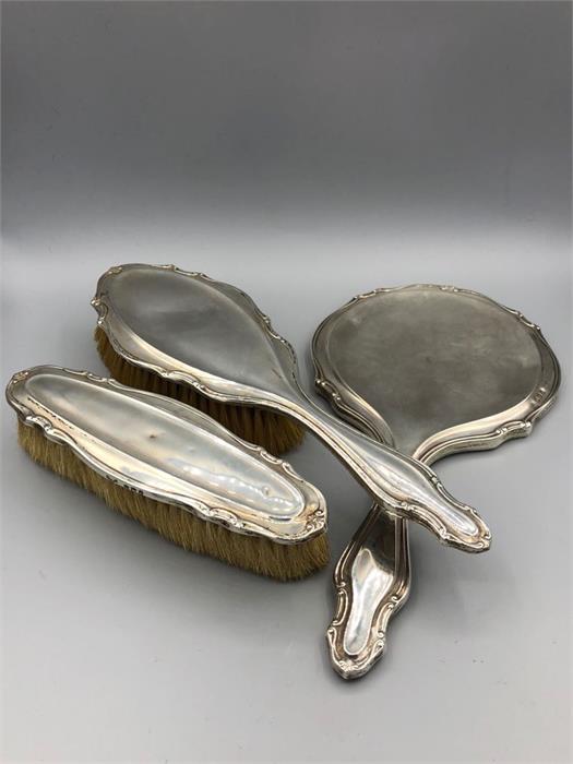 A hallmarked silver backed ladies dressing table set, comprising a hand mirror and two brushes.