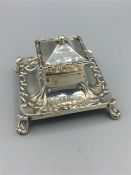 A silver square lidded inkstand, turned out feet to each corner, repousse scroll work around top and