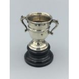 A silver hallmarked miniature two handled presentation cup on an ebonised wooden stand