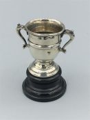 A silver hallmarked miniature two handled presentation cup on an ebonised wooden stand