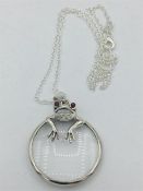 A silver magnifying glass in the form of a frog with ruby eyes