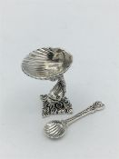 A silver salt and spoon with dolphin style base