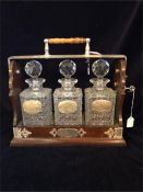A Tantilus with three cut glass decanters and hallmarked silver labels with a hunting theme,