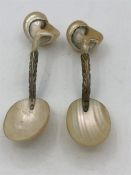 A pair of shell spoons on white metal mounts