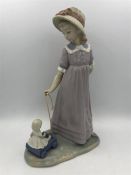 A Lladro figure of a girl with a doll in a cart.