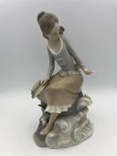 A Lladro figure of a young lady on a rock