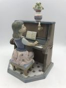 A Lladro figure of a young girl playing piano.