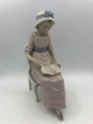 A Lladro figure of a seated girl reading her book.