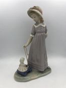 A Lladro figure of a girl playing with her doll in a cart.