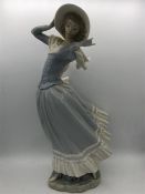 A Lladro figure of a windswept lady in a hat.