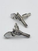 A pair of silver cuff links in the form of pistols with mop handles.
