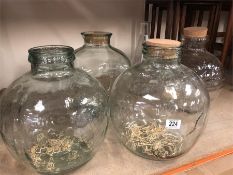 Four large glass jars with corks and a large measuring jug, scientific style.