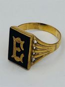 A 9ct yellow gold gents ring with a central E on black stone. (5.1g)