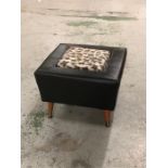 A Mid Century Black footstool with leopard print inset on teak legs with brass feet.