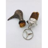 Two white metal bottle stoppers, a Birds head and a Mercedes Benz symbol.