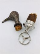 Two white metal bottle stoppers, a Birds head and a Mercedes Benz symbol.