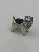 A sterling silver pincushion in the form of a dog with ruby eyes and emerald stone collar.