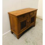 A light oak sideboard with two drawers and carved cupboard doors in an Arts and Crafts style