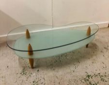 A Contemporary kidney shaped coffee table on three legs with a frosted glass lower shelf.