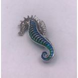 A silver and enamel sea horse shaped brooch with ruby eye
