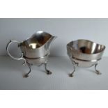 An Edwardian silver cream jug and matching sugar bowl with central band decoration and hoof feet