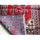 An Afghan hand-knotted burgundy-ground Balochi wool rug with multi-coloured isometric designs,