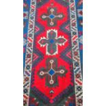An Oriental hand-knotted wool rug with multicoloured isometric designs. double border and medium