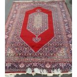 An Oriental hand-knotted multi coloured burgundy-ground wool rug with double border and long fringe,