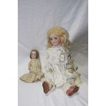 Two bisque headed dolls Comprising a large doll with long blond wig, fixed blue eyes, open mouth,