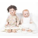 Two German bisque headed dolls Comprising a doll with curly brown wig, open/shut brown eyes,