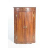 A George III mahogany bowfront hanging corner cupboard Having a frieze inlaid with brass stringing