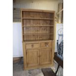 A Victorian pine kitchen dresser Having three adjustable enclosed shelves above a pair of frieze