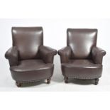 A pair of brown leather easy chairs, early 20th Century Having a padded back and padded out swept