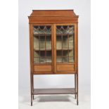 An Edwardian inlaid mahogany display cabinet Having a shaped pediment above a frieze inlaid with