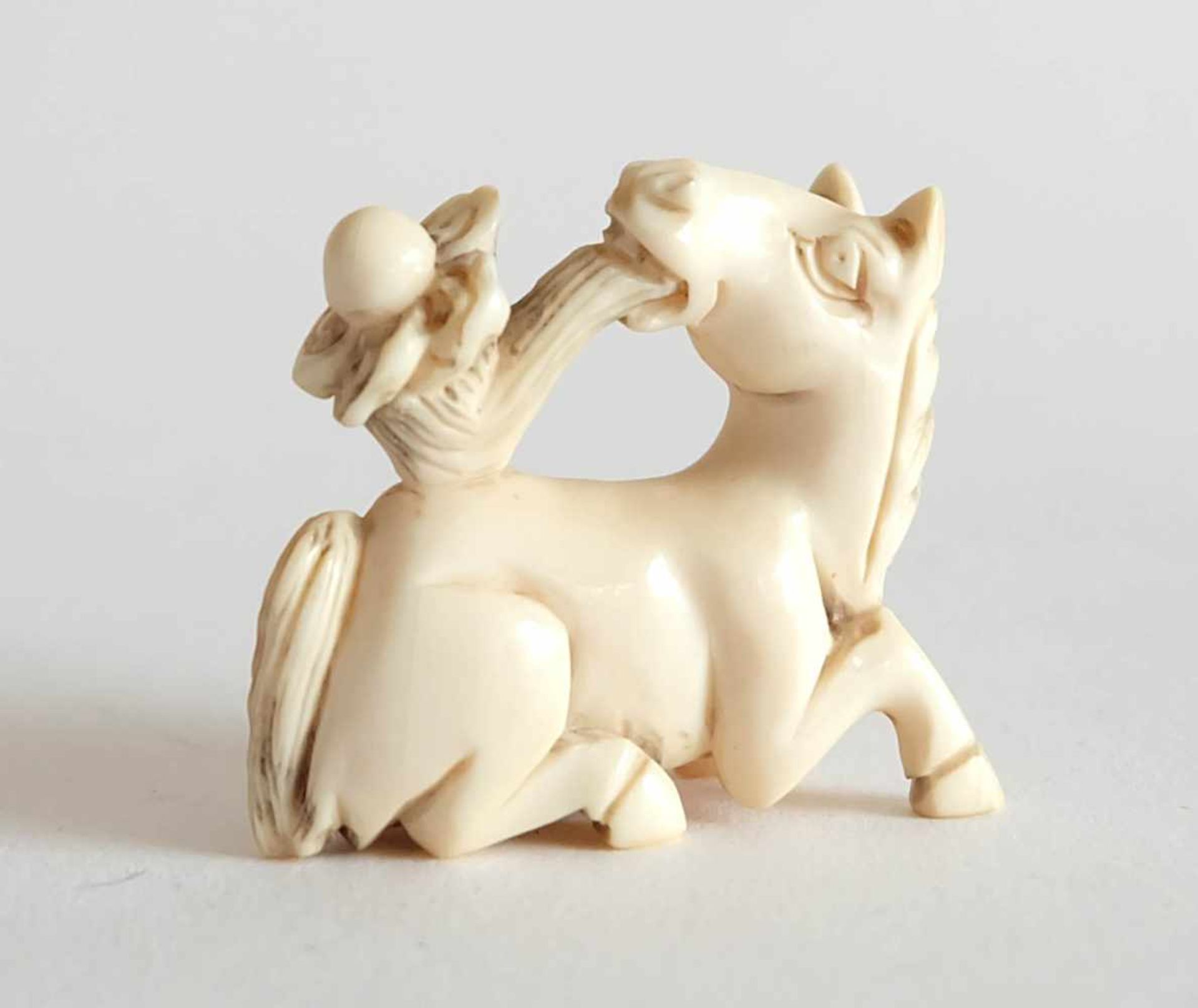 NETSUKE, Japan, 19./ 20.Jh., Elfenbein, Pferd mit ewiger Perle in Blütenkelch, 3,4 x 4,4 cm