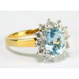 An 18ct yellow gold ring set with central oval cut light blue stone surrounded by twelve small